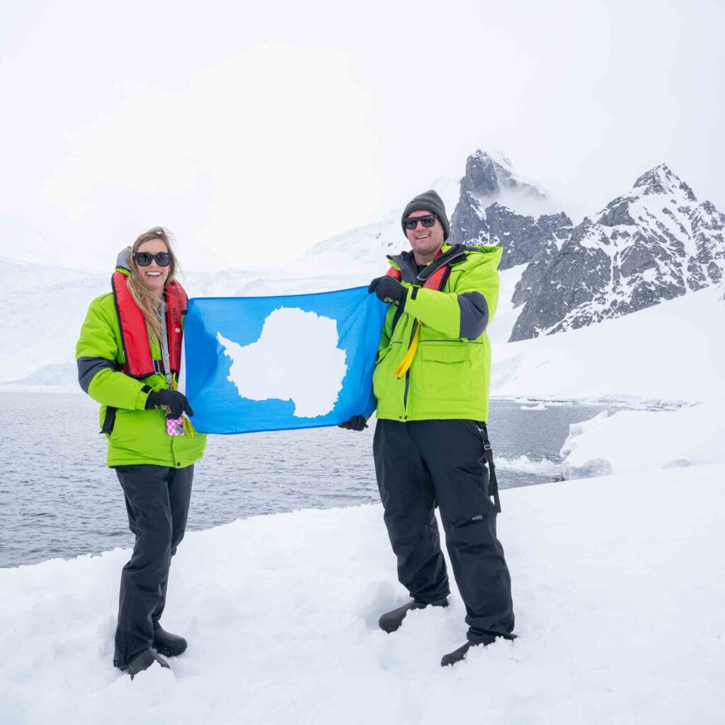 couple holding the Antarctic Flag on the first continental landing of an Antarctica Cruise in Orne Harbor